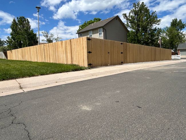 A wooden fence is sitting on the side of a road next to a house.