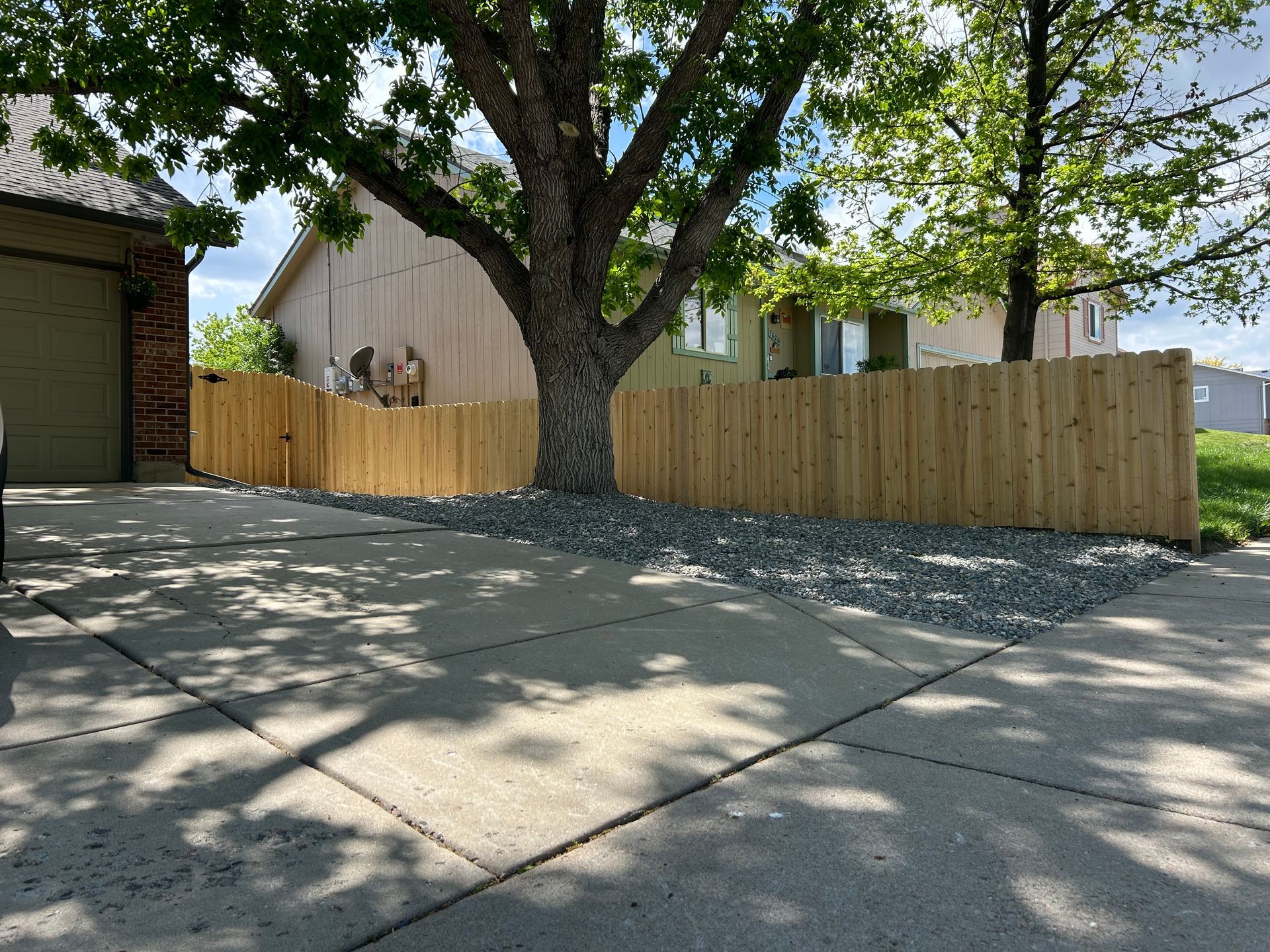 A wooden fence is surrounding a tree in front of a house.