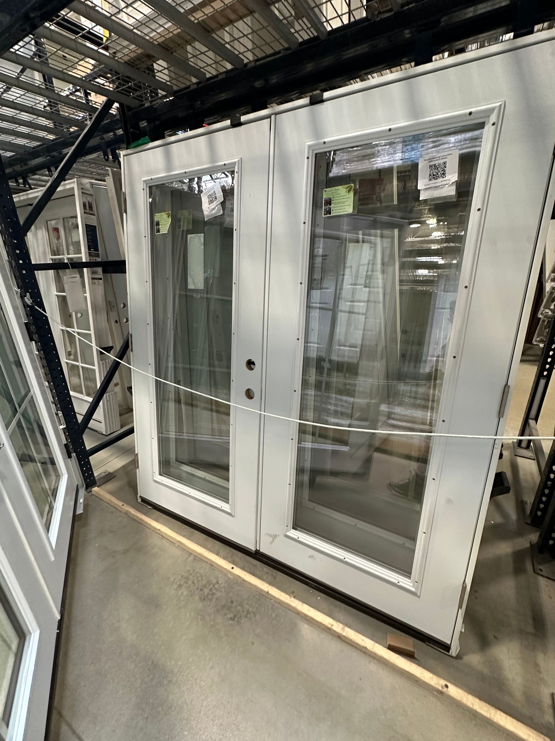 A pair of white sliding glass doors are sitting on top of a concrete floor in a warehouse.