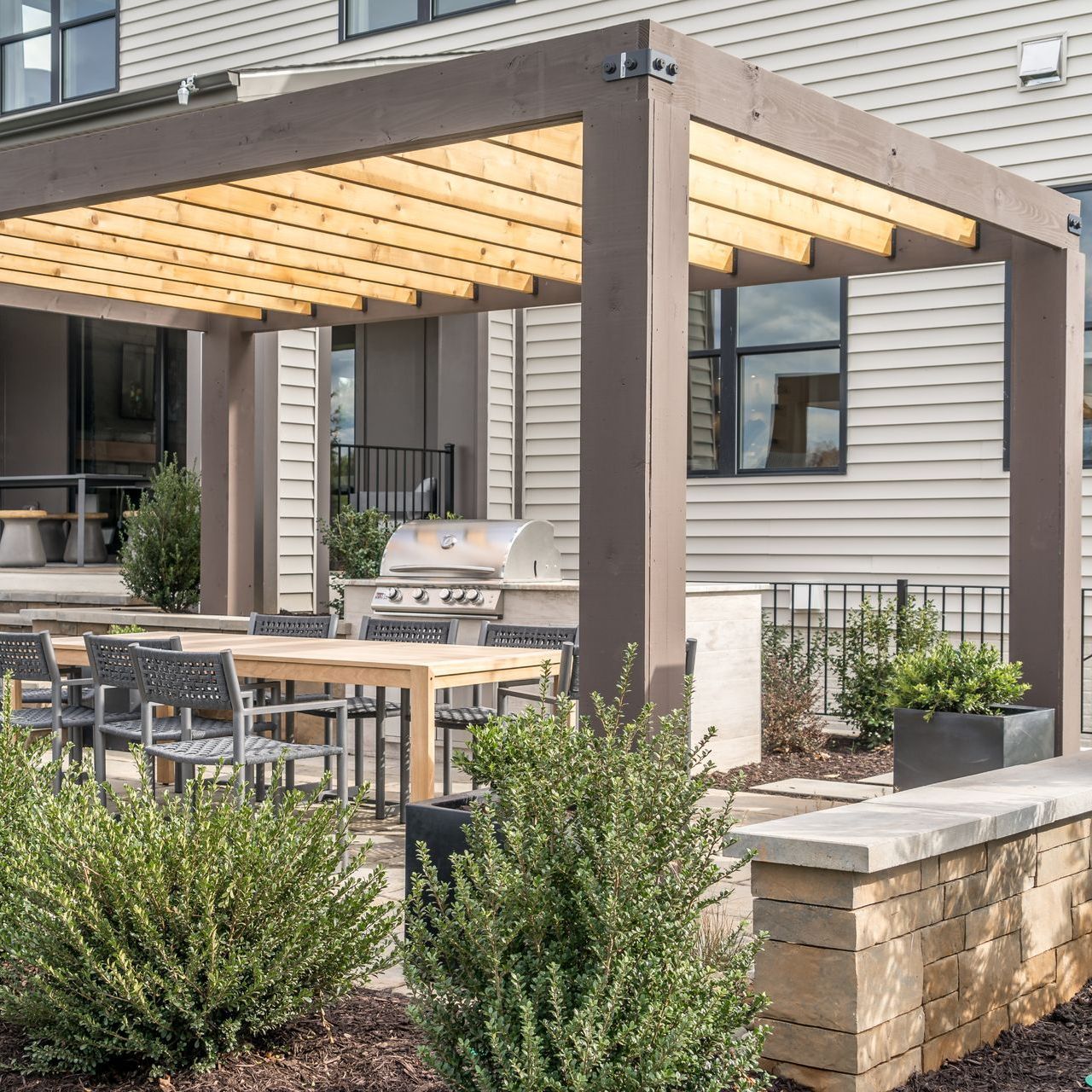 A pergola with a table and chairs underneath it in front of a house.