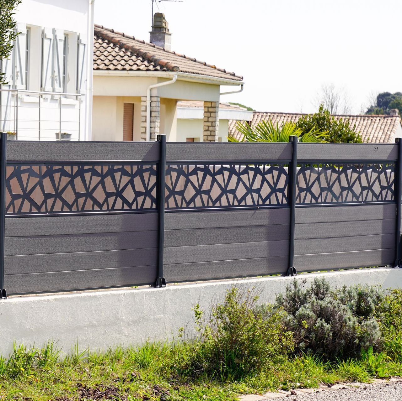 A fence with a pattern on it is in front of a house.
