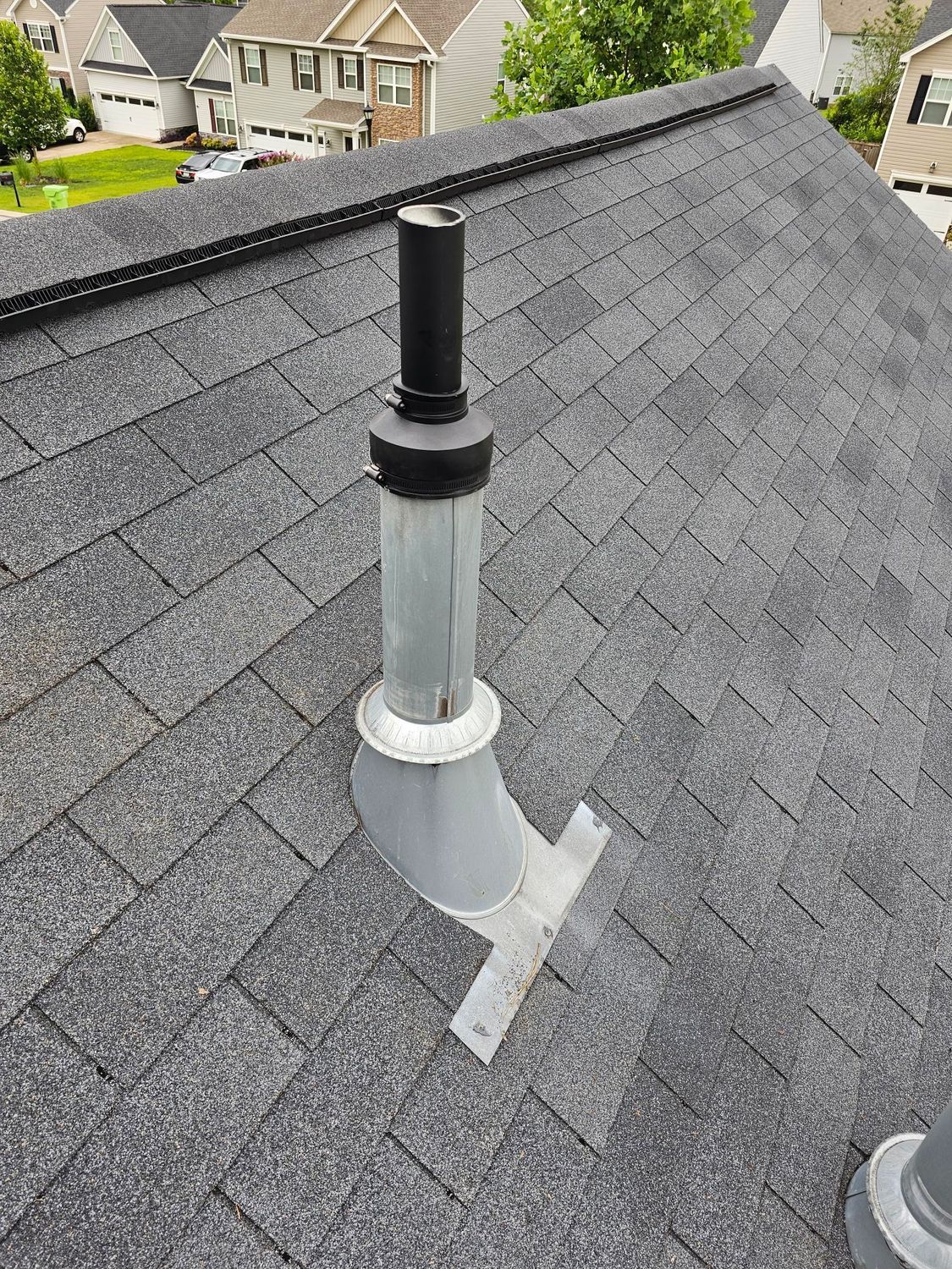 A roof with gray asphalt shingles. A metal vent pipe with a black cap protrudes.