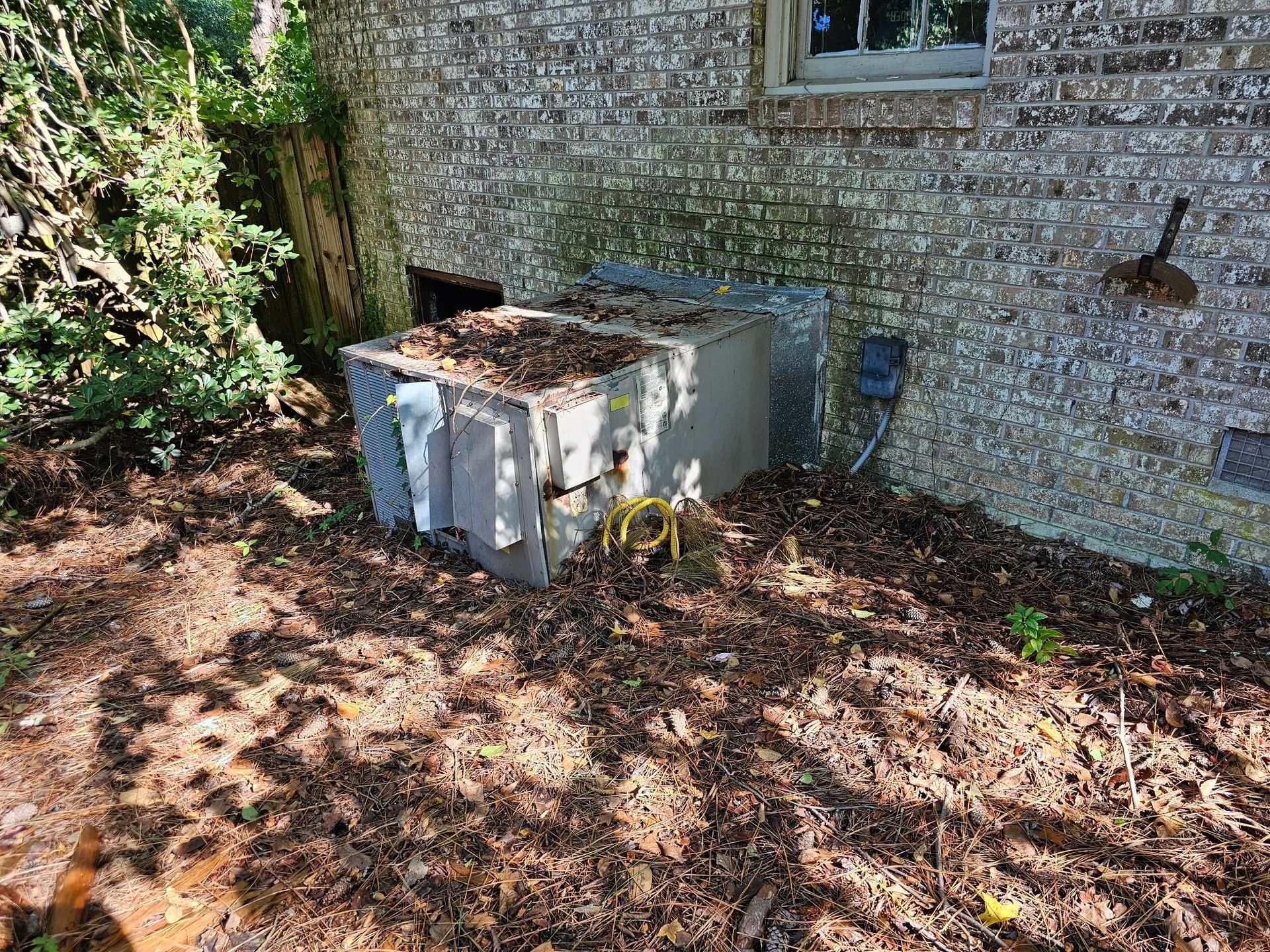 Outdoor air conditioning unit covered in debris next to a brick wall.