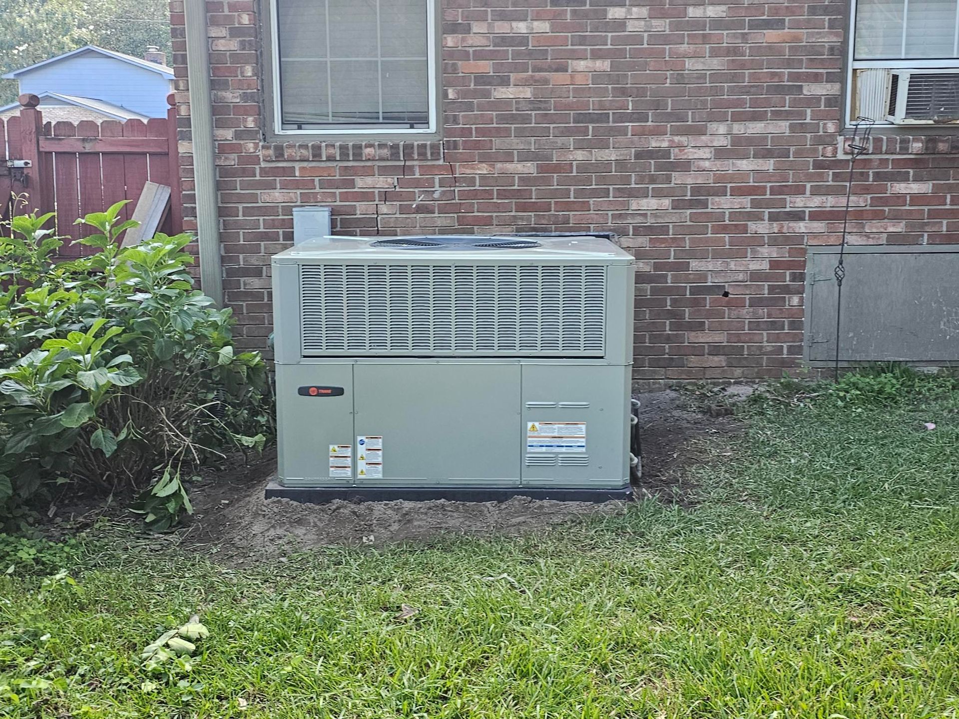 Air conditioning unit, light green, against a brick wall, outdoors.