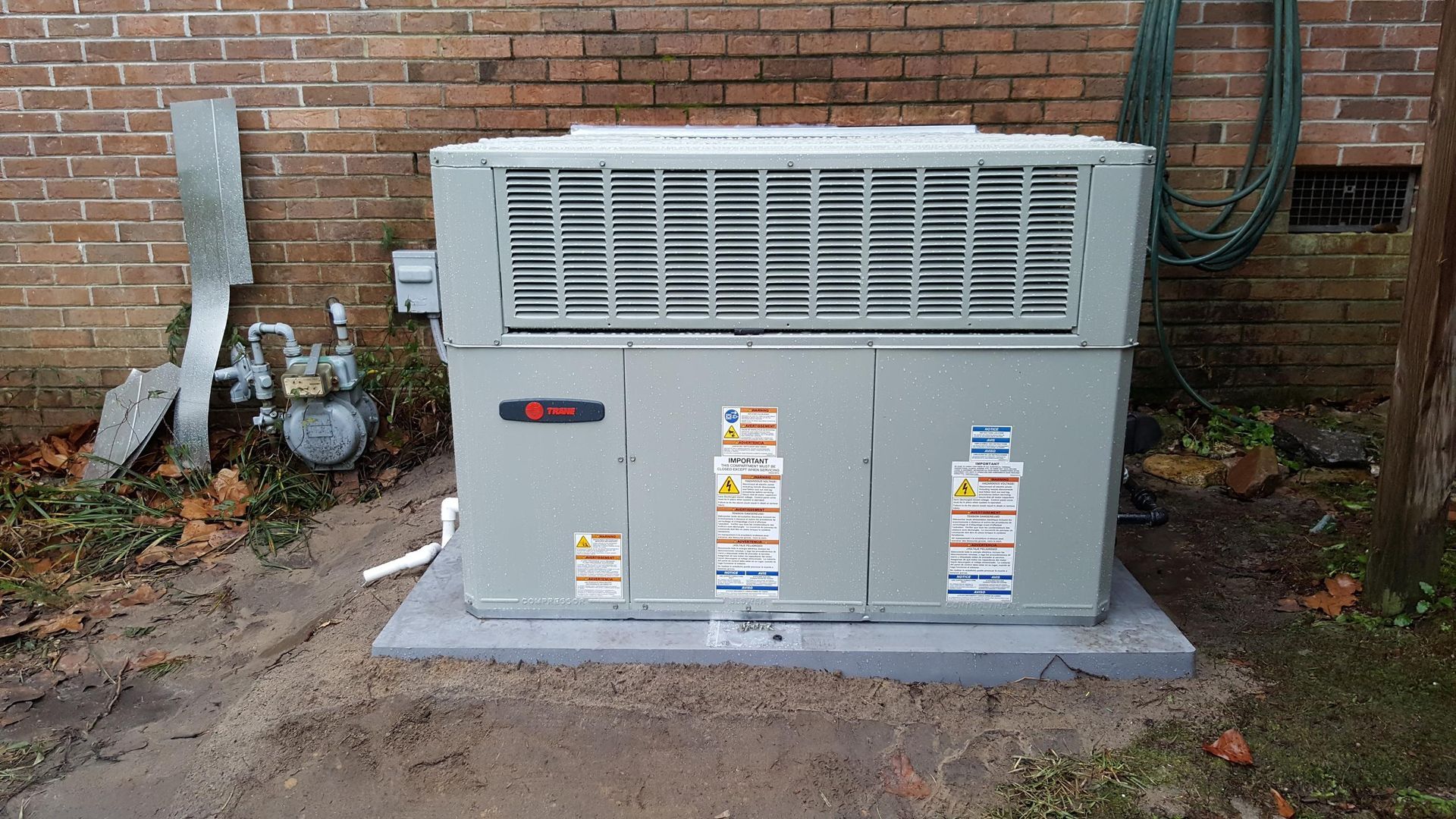 A Trane HVAC unit on a concrete pad next to a brick wall.
