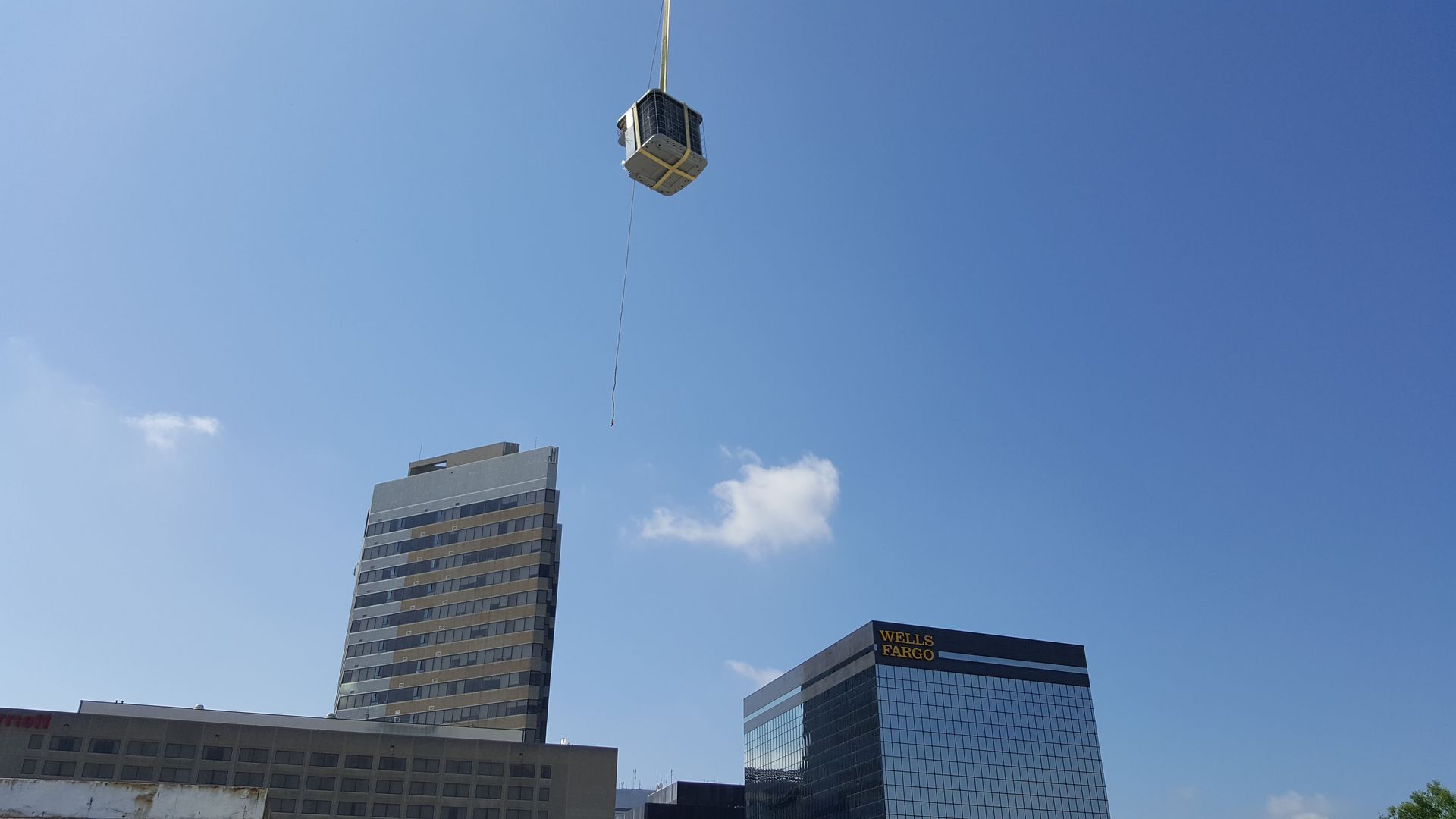 Crane lifting a small metal container above city buildings against a blue sky.