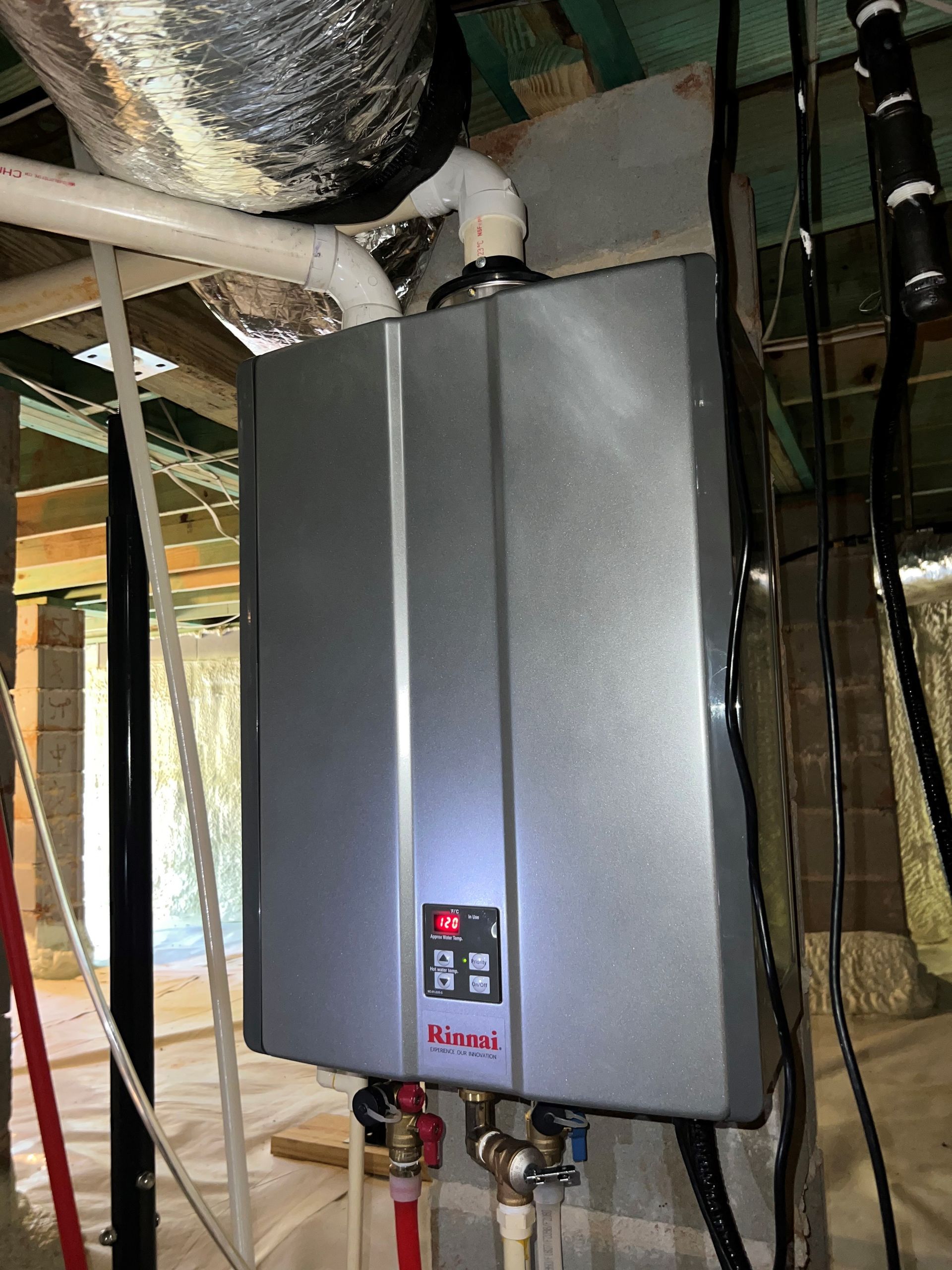Tankless water heater in a basement setting. Gray unit with red and brass plumbing.