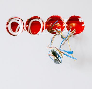 Four red electrical junction boxes on a white wall; wires extend from the boxes.