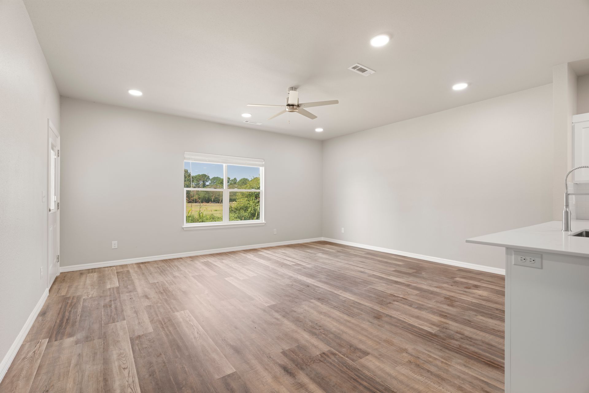 An empty living room with hardwood floors and a ceiling fan.