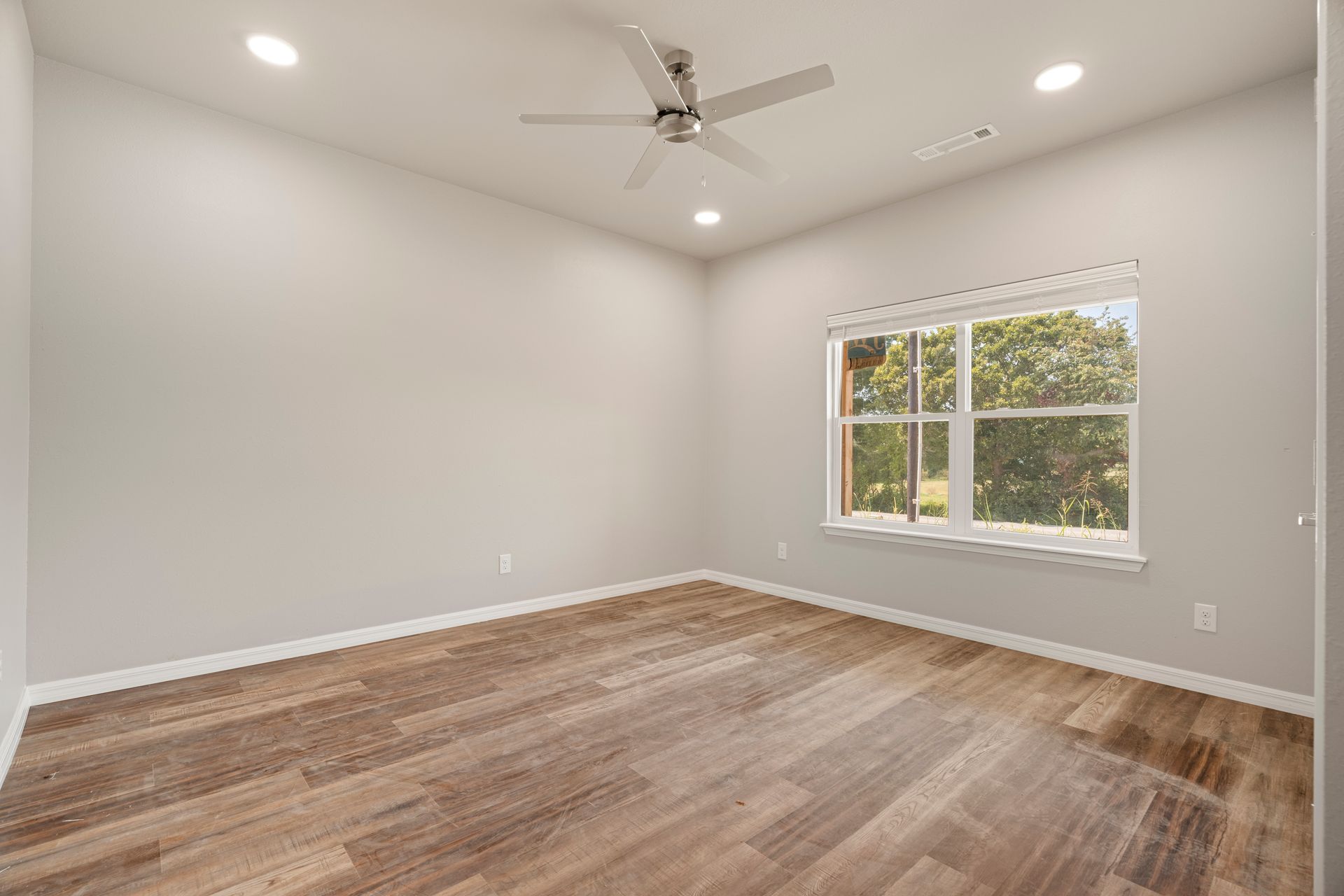 An empty bedroom with hardwood floors and a ceiling fan.