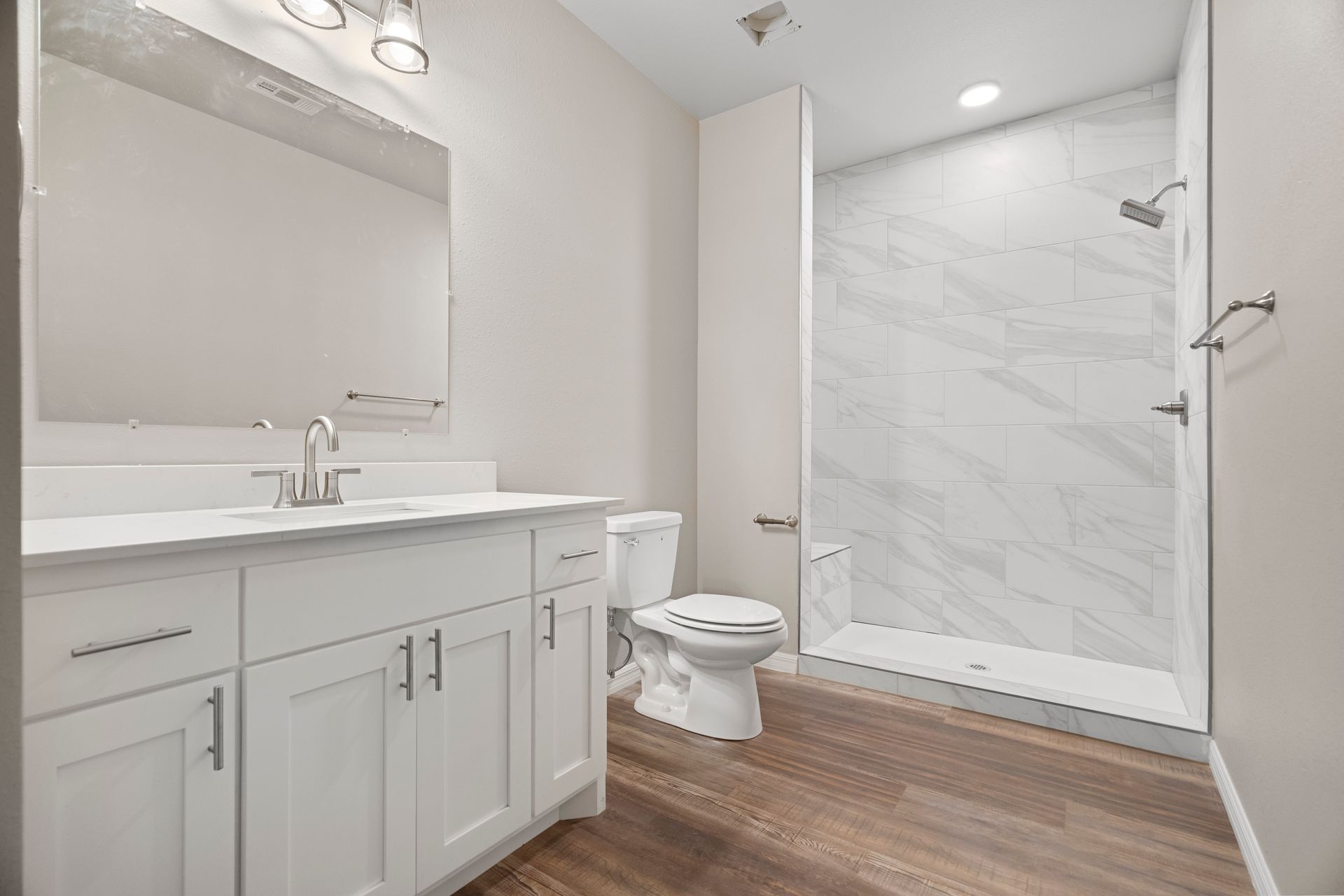 A bathroom with a toilet , sink , mirror and walk in shower.