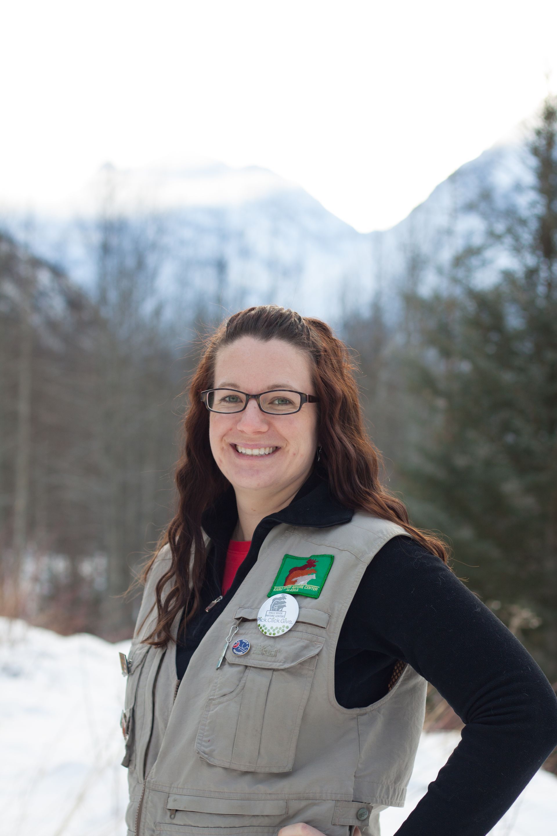 A woman wearing glasses and a vest is standing in the snow.