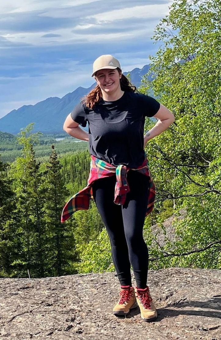 A woman is standing on top of a mountain with her hands on her hips.