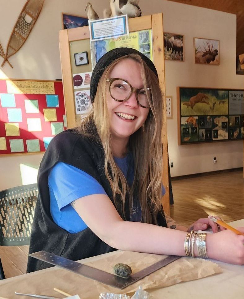 A woman wearing glasses and a hat is smiling while sitting at a table