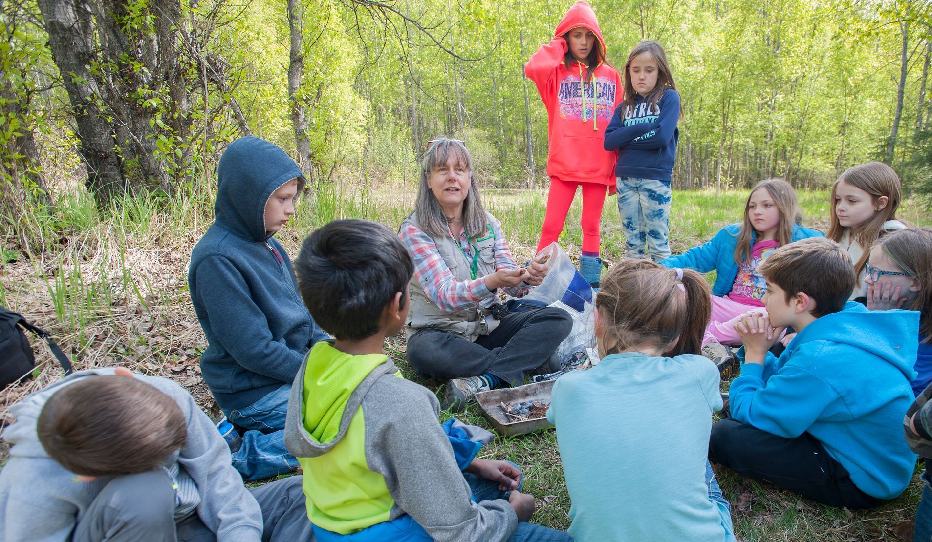 A group of children are sitting in a circle in the woods.