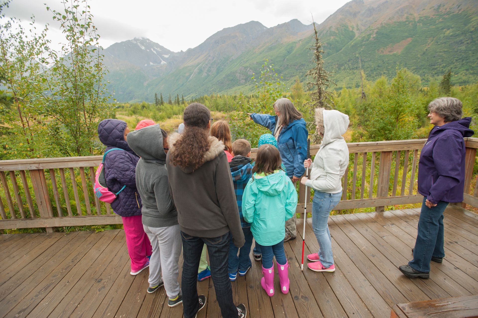 A group of children are standing on a deck looking at mountains.
