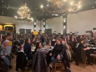 A large group of people are sitting at tables in a room holding up signs.