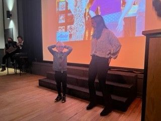A woman and a child are standing on a stage in front of a large screen.