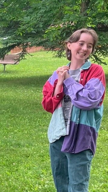 A woman in a colorful jacket is standing in the grass in a park.