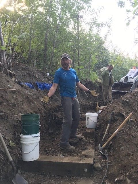 A man is standing in a pile of dirt next to buckets and shovels.