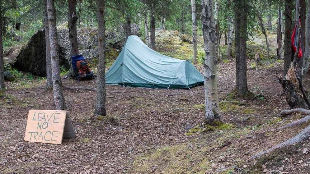 A tent is sitting in the middle of a forest next to a sign that says leave no trace.