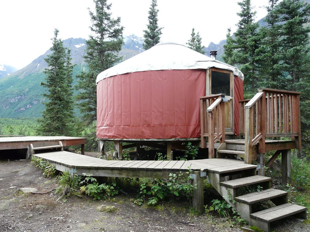 A red yurt with a wooden deck and stairs in the woods
