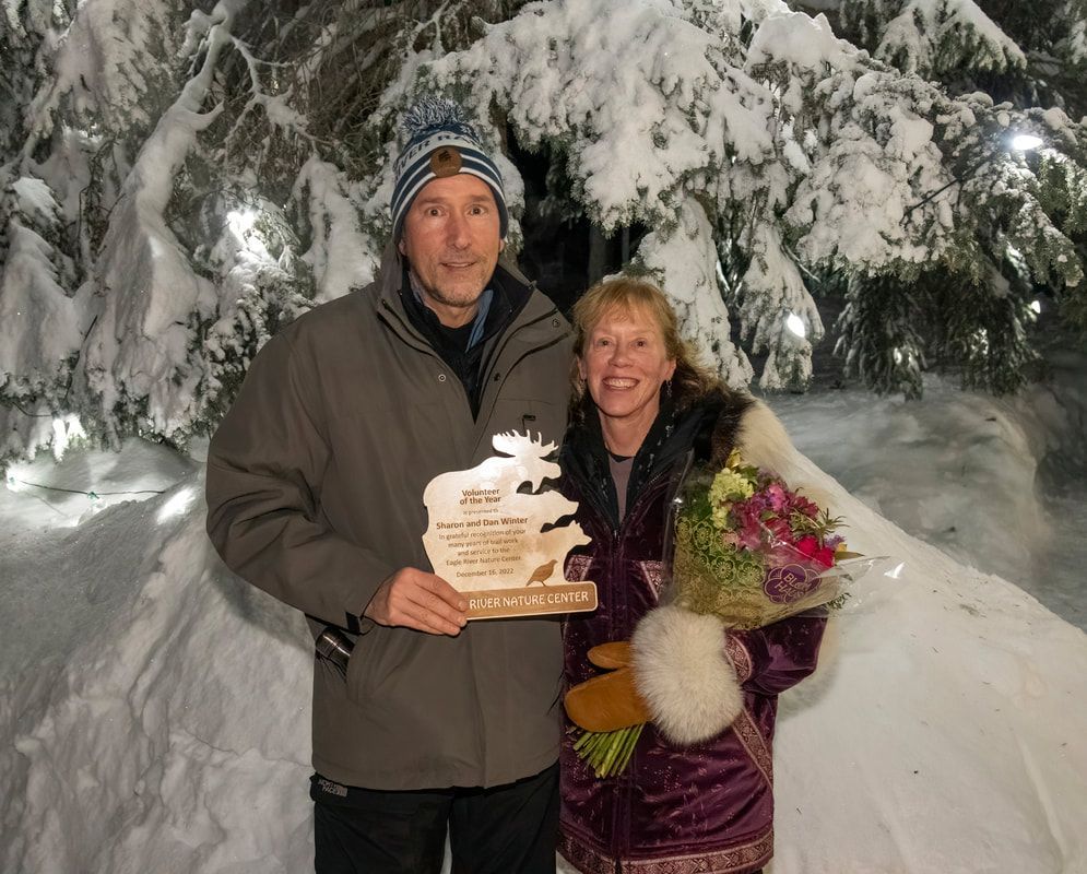A man and woman standing in the snow holding a trophy
