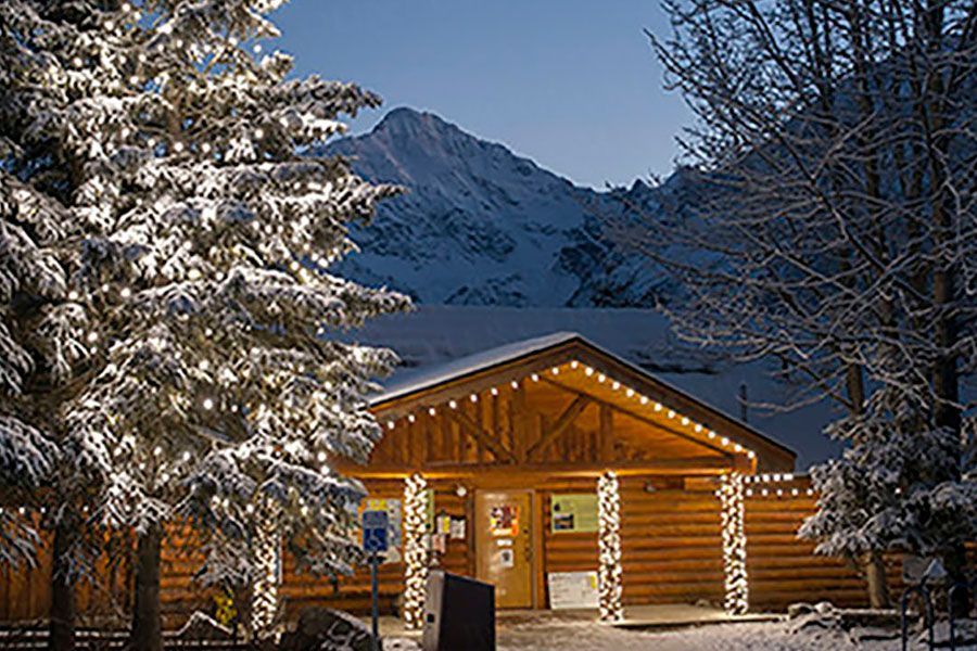 A log cabin covered in snow with a mountain in the background.