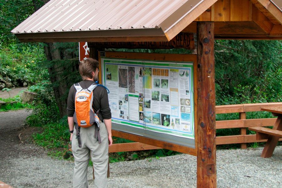 A man with an orange backpack is looking at a bulletin board.