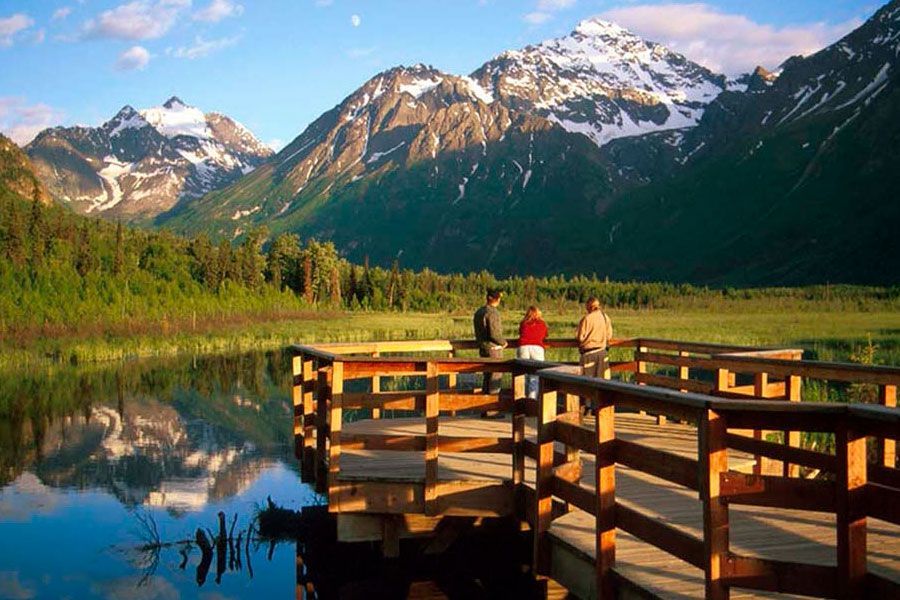 A couple of people standing on a dock overlooking a lake with mountains in the background