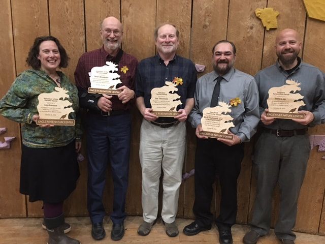 A group of people holding trophies in front of a wooden wall