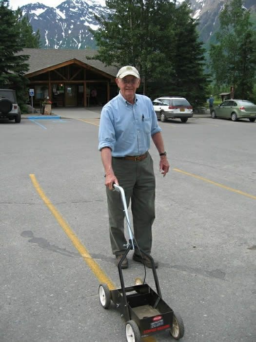 A man is pushing a lawn mower in a parking lot