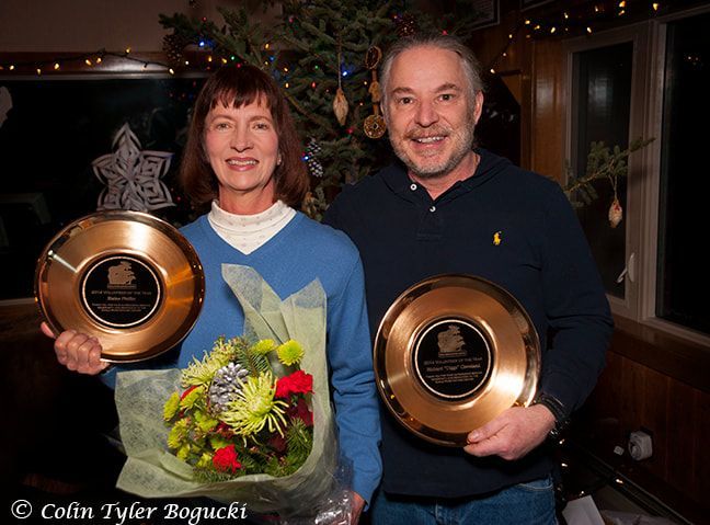 A man and a woman holding plaques and flowers in front of a christmas tree