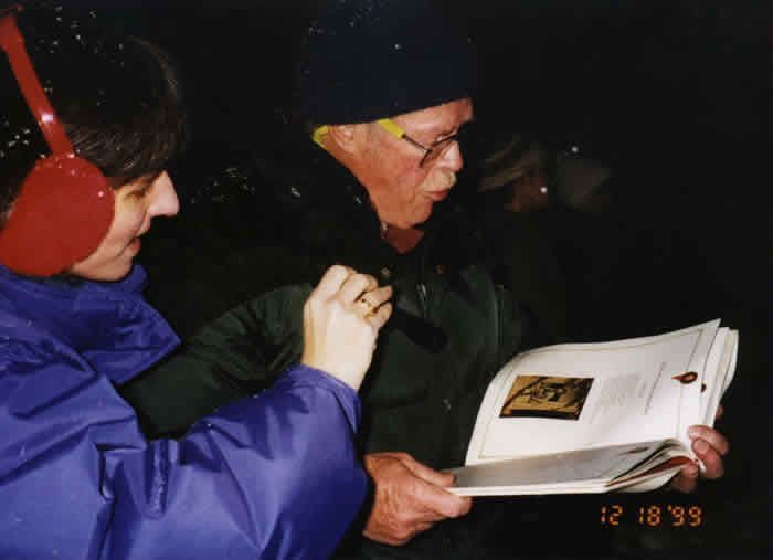A man wearing headphones is reading a book to another man