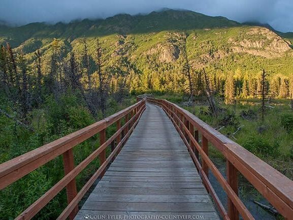 A wooden bridge over a river with mountains in the background.
