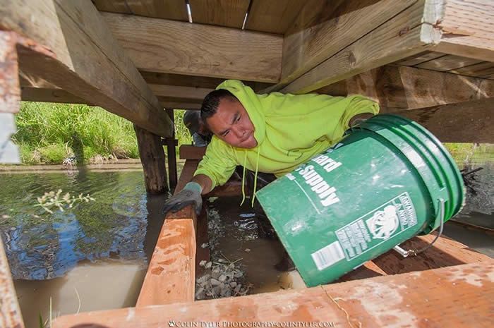 A man is holding a green bucket under a bridge.