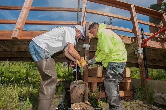 Two men are working on a wooden bridge.