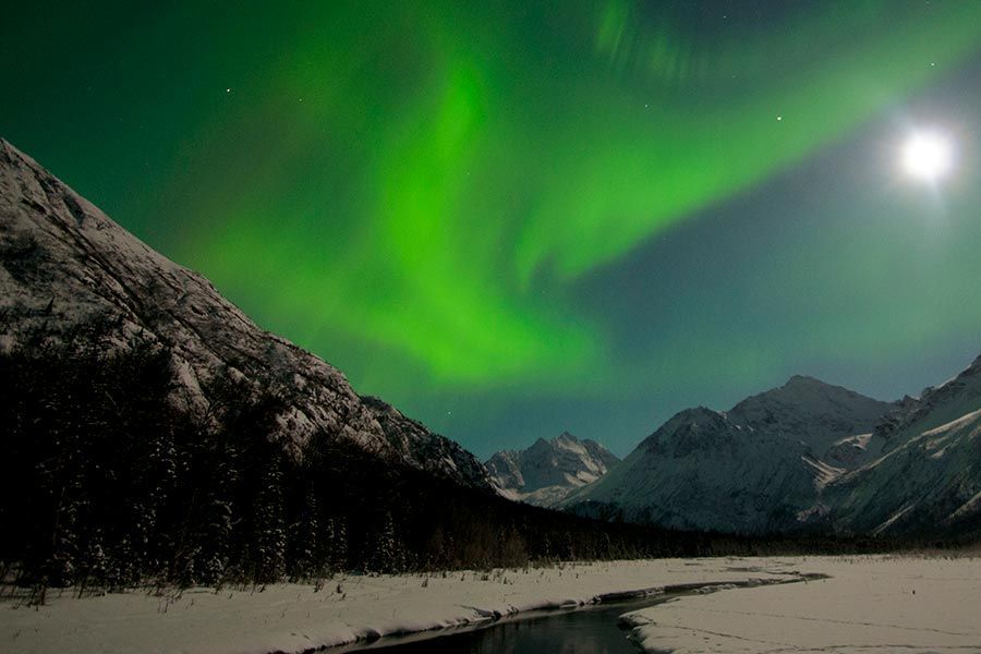The aurora borealis is dancing over the mountains and a river.