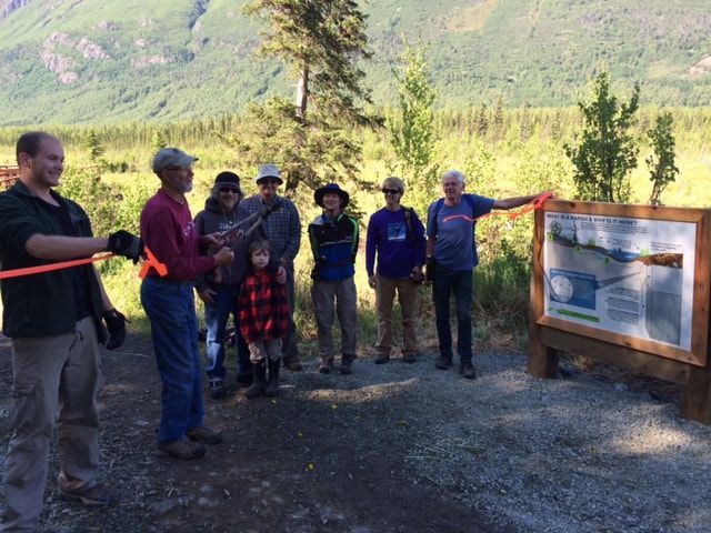 A group of people are standing around a sign in the woods.