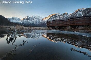 A wooden bridge over a body of water with mountains in the background.