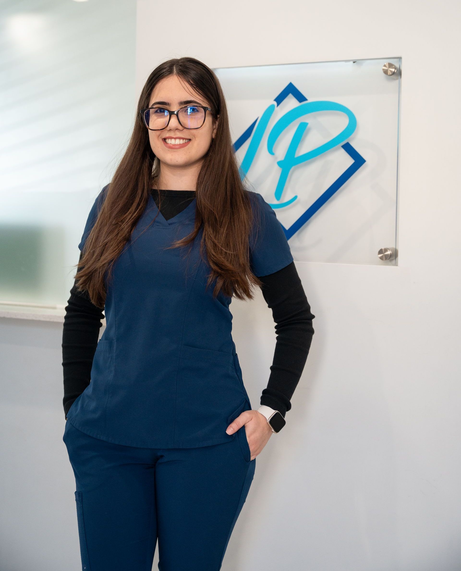 A woman in a blue scrub is standing in front of a sign with the letter p on it