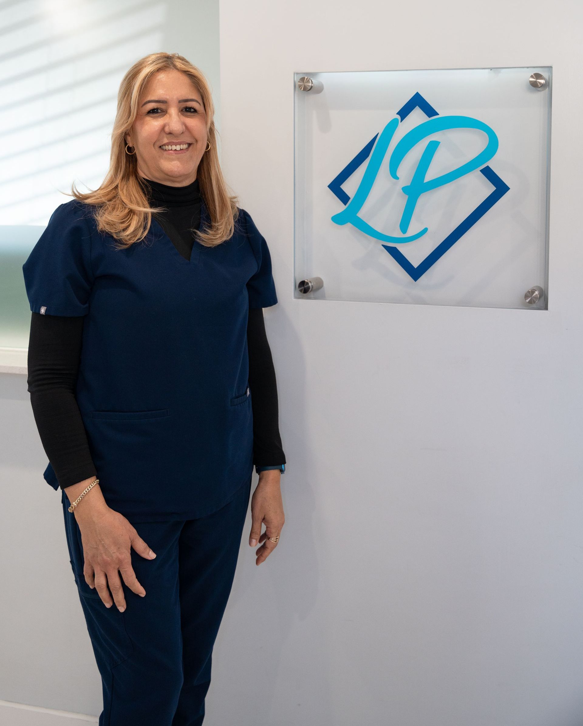 A woman in a blue scrub top is smiling for the camera.