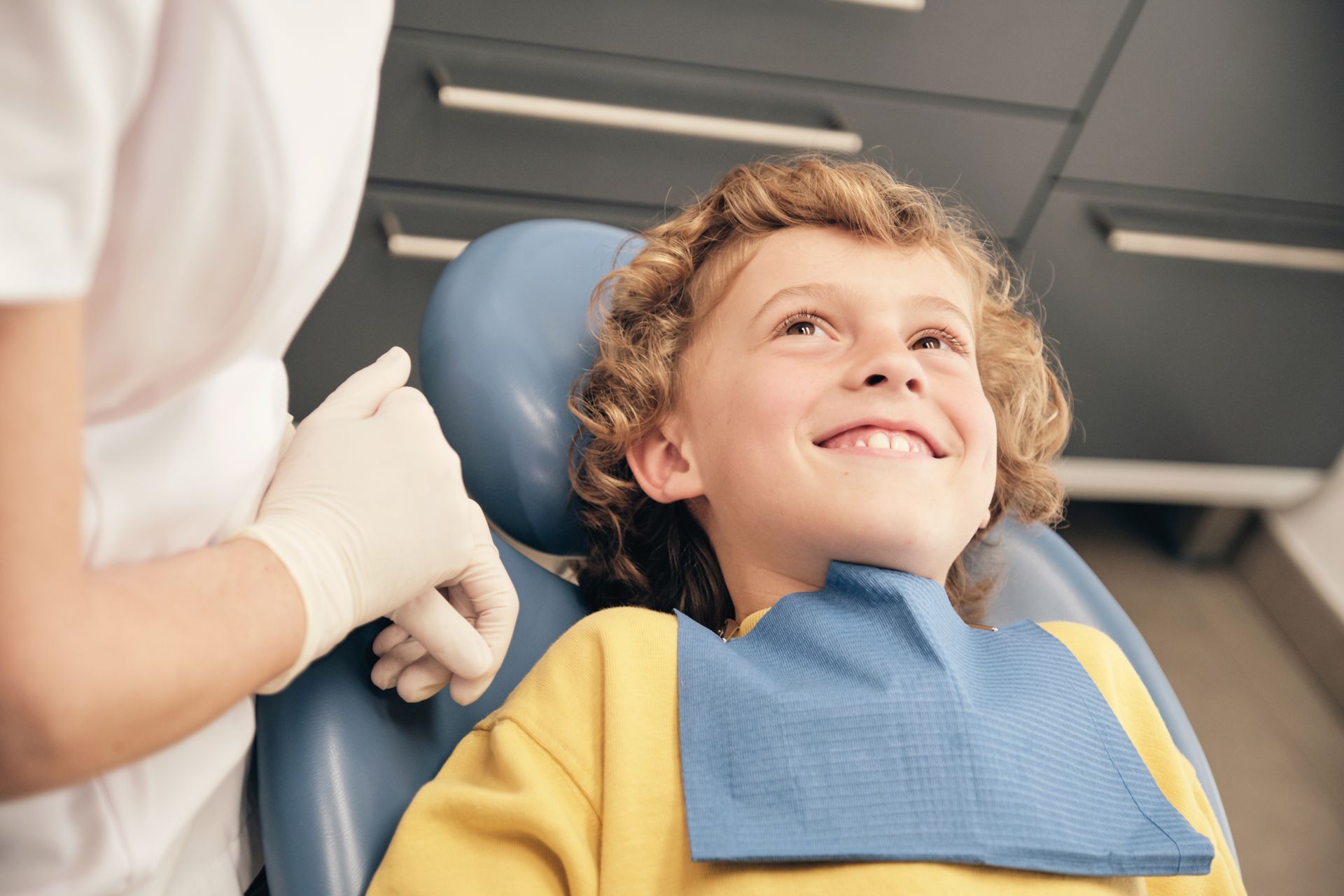 A young boy is sitting in a dental chair and smiling.