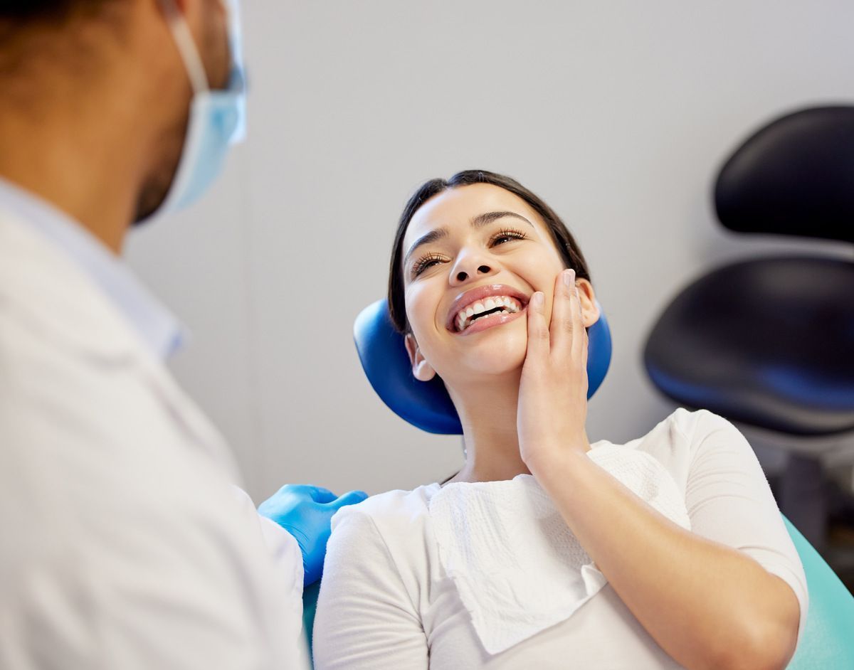 Dentist speaking with a smiling patient in a clinic chair, patient touching her cheek