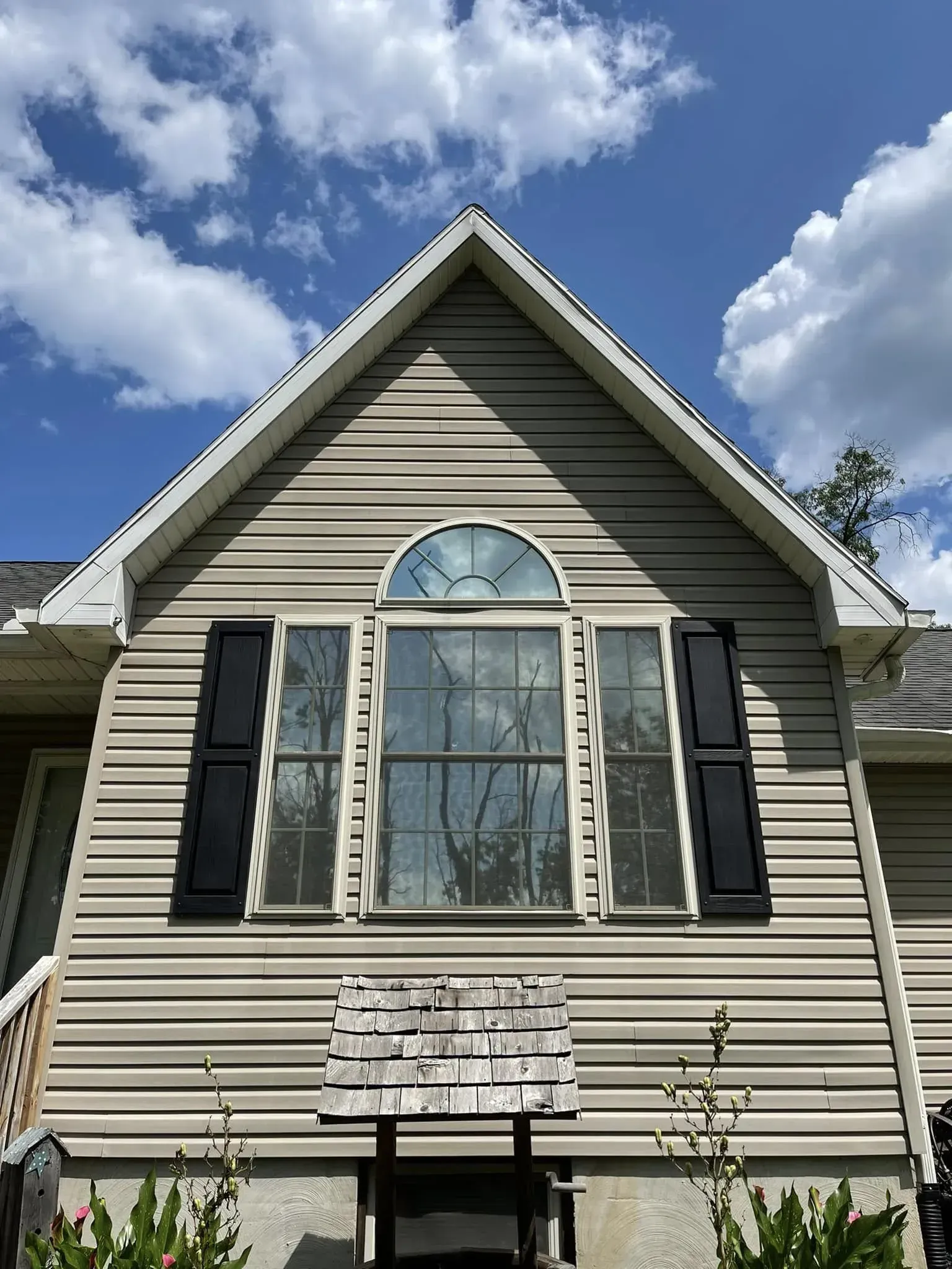 Tan house exterior with arched window, black shutters, and cloudy blue sky.