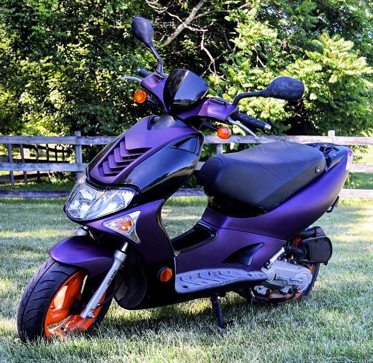 Purple and black scooter parked on grass.