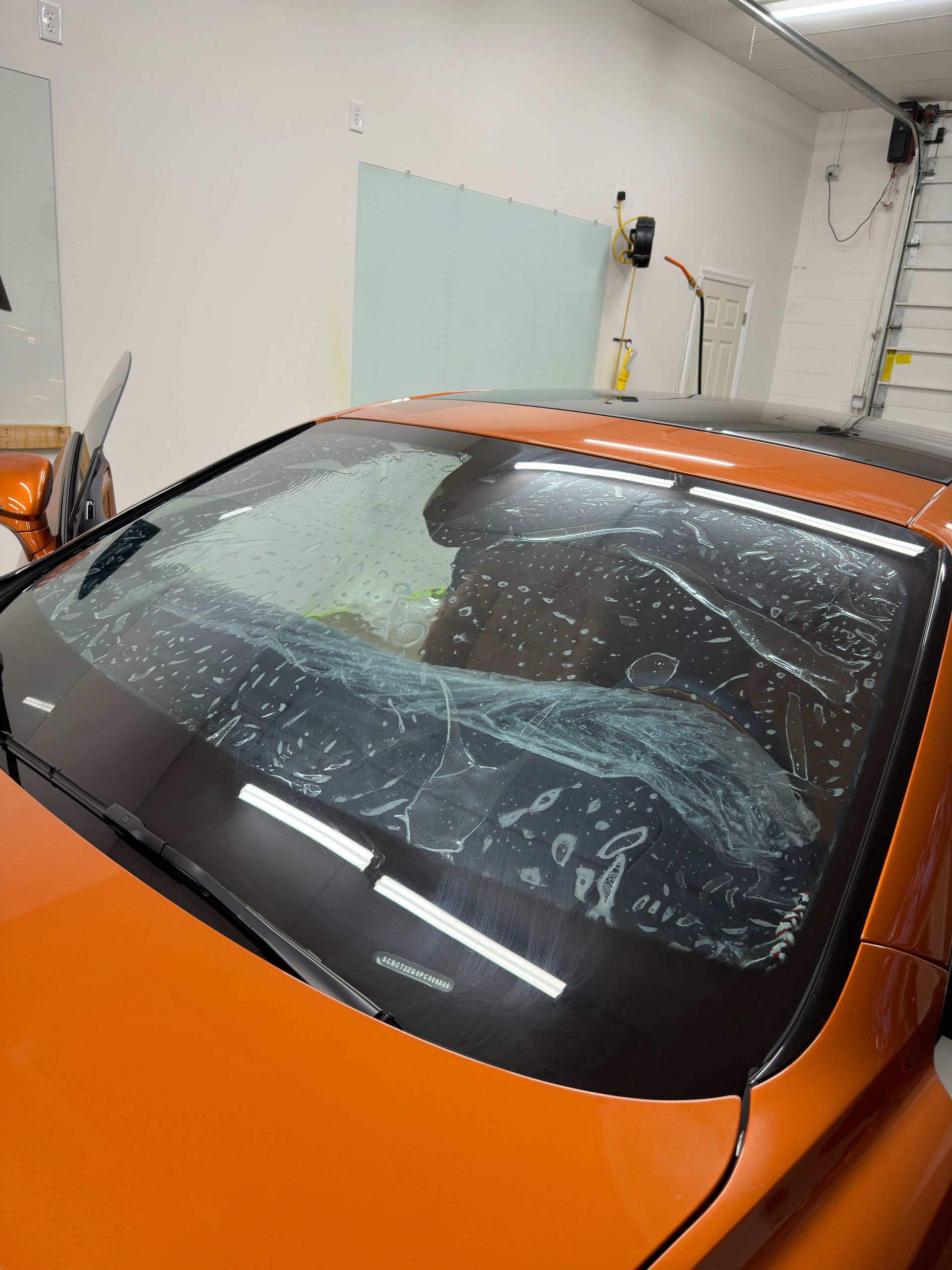 Orange car windshield with clear protective film being applied indoors.