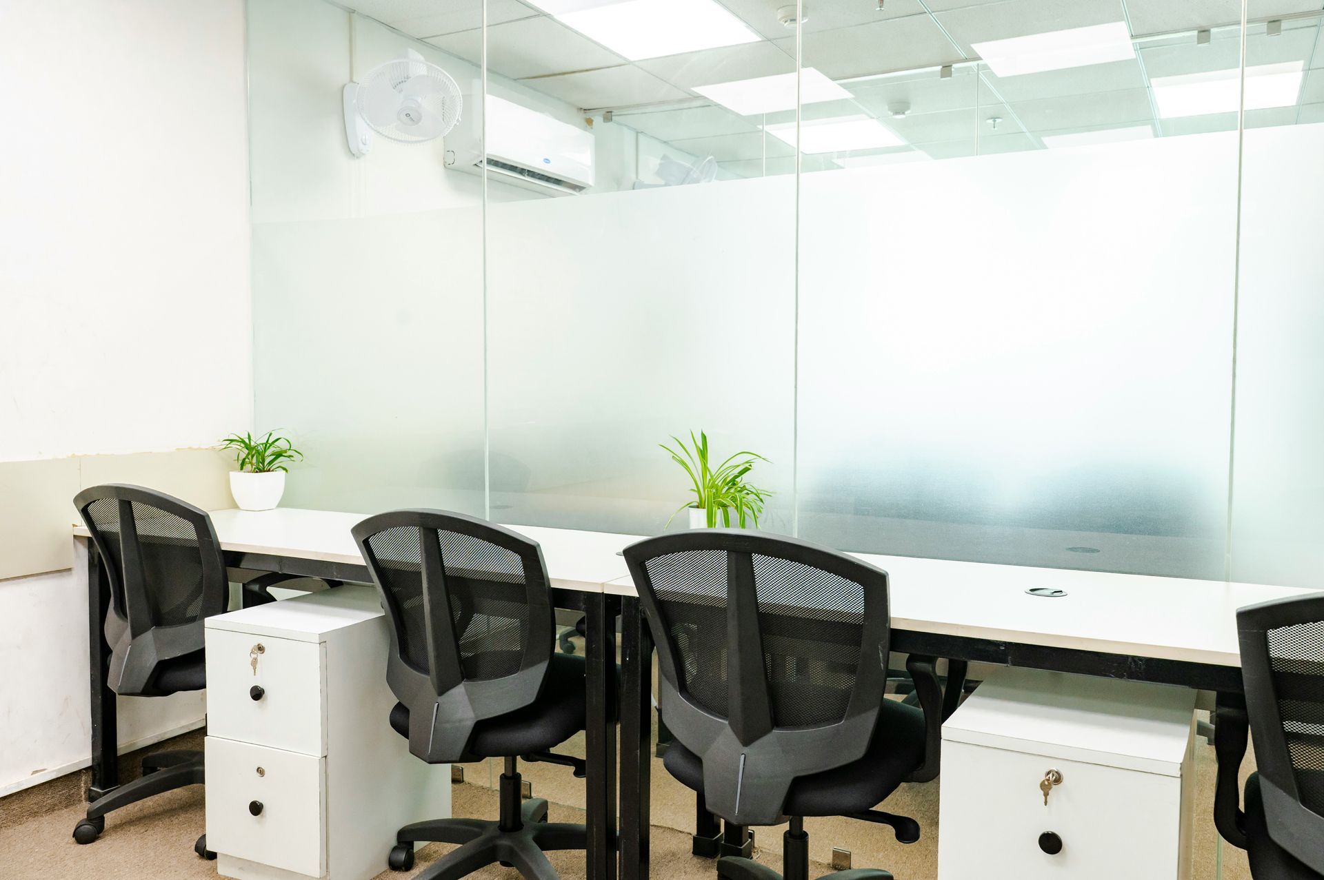 A modern office with white desks, black chairs, and frosted glass walls.