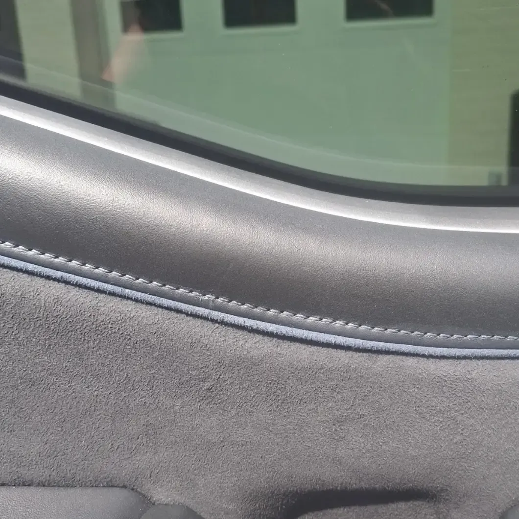 Gray car door interior with stitching detail and a window.