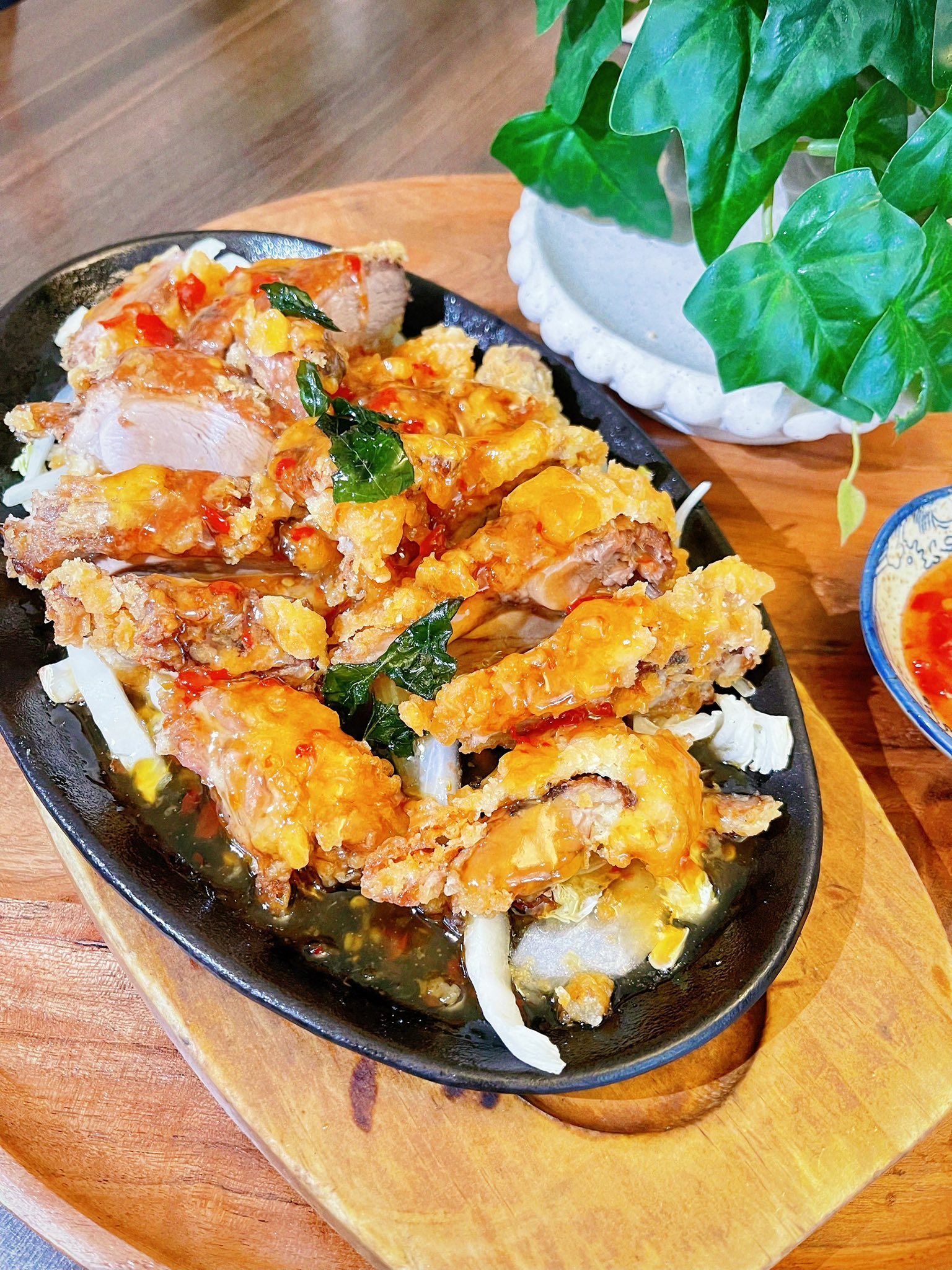 Fried chicken dish on a sizzling platter, garnished with herbs and sauce, served with a small bowl of chili sauce— L'il Buddha Asian Cuisine in Salamander Bay, NSW